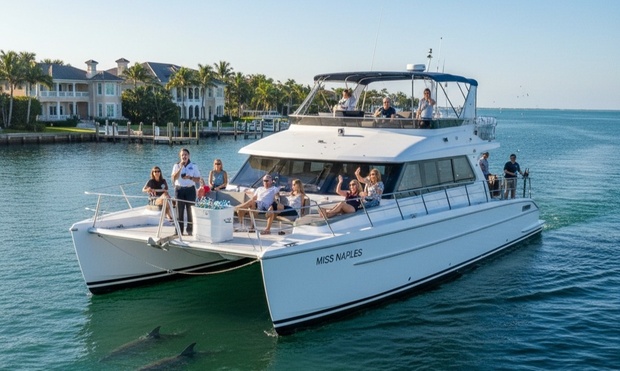 A white catamaran cruising on the water with a city skyline in the background.