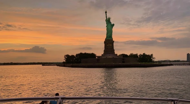 The Statue of Liberty at sunset with the NYC skyline in the background.