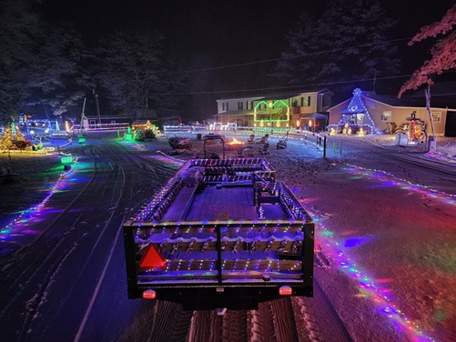 A car driving through a festive Christmas light display at a campground at night.