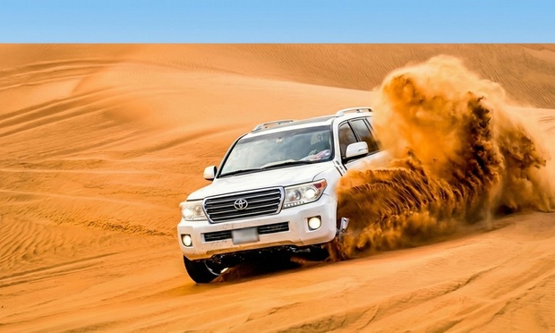 A 4x4 vehicle kicking up sand during dune bashing in the desert at sunset.