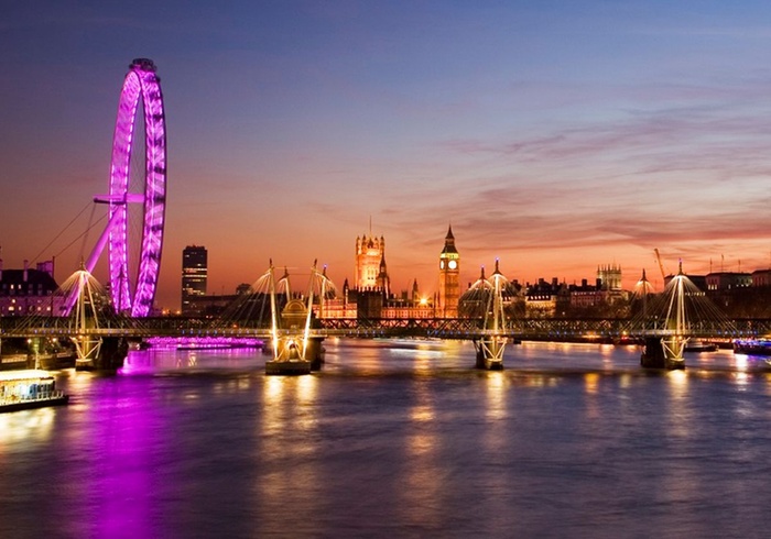 A river cruise vessel sailing past London's illuminated Parliament and Big Ben at dusk.