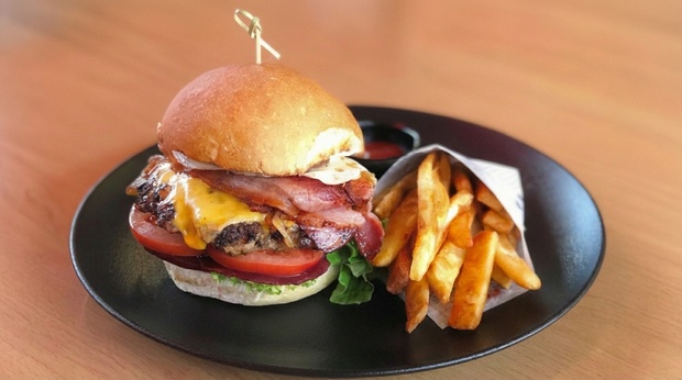 Overhead view of various pasta and burger dishes, drinks, and desserts at City Extra with a hint of waterfront background.