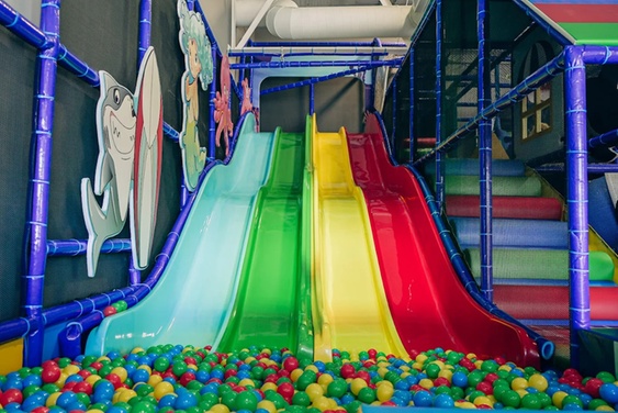 A vibrant indoor playground with colorful slides, climbing structures, and soft play areas.