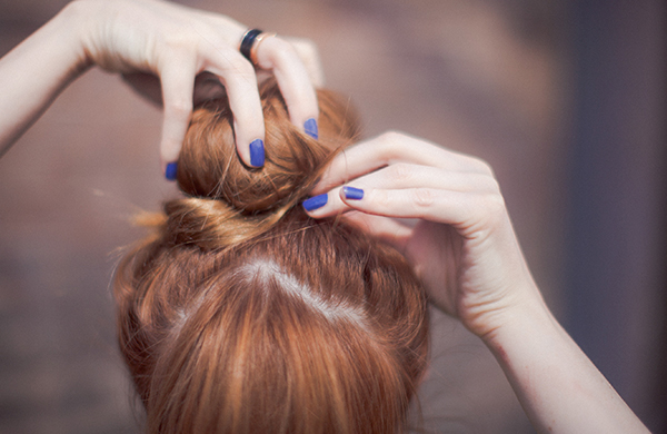 Red-haired woman tying up hair in a bun updo