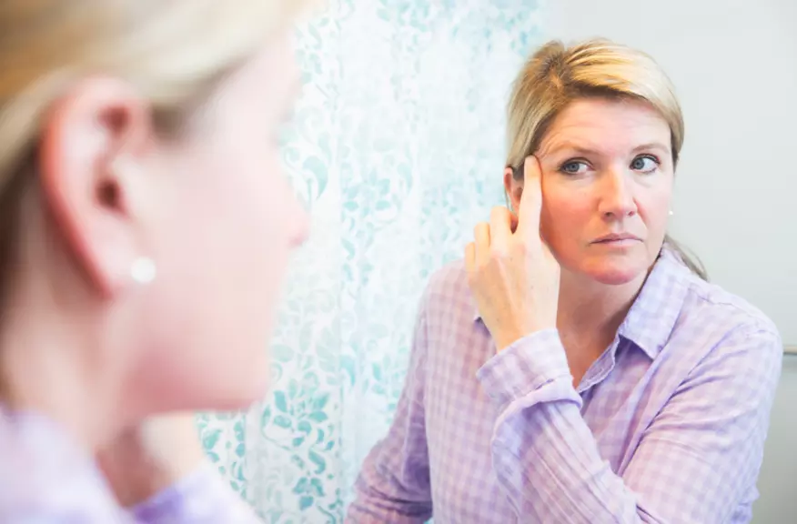 woman looking at wrinkles in the mirror