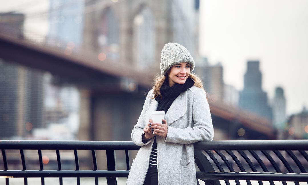 Woman in stylish winter attire leaning against snowy railing