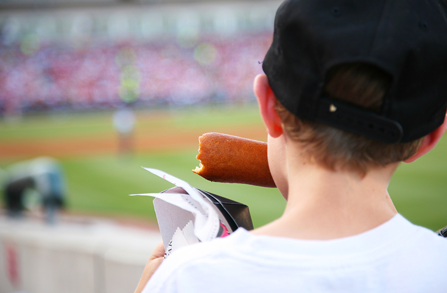 kid eating a corn dog at a baseball game