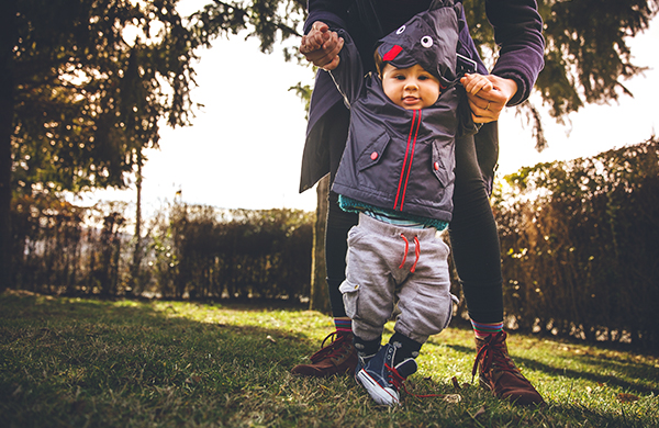Young toddler holding hands with parent and learning to walk