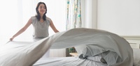 woman fluffing sheets while making the bed