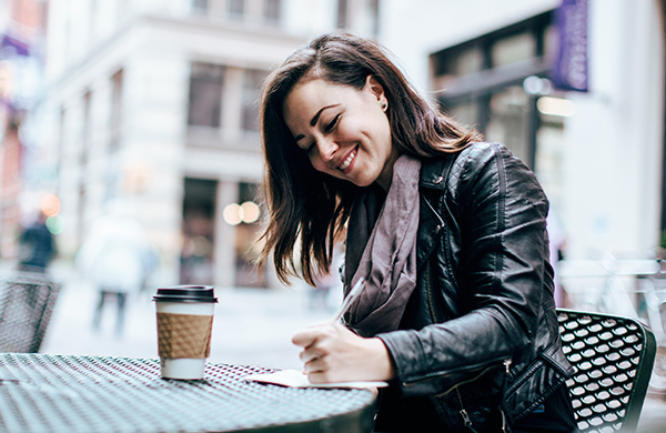 woman writing in a journal and drinking coffee jpg